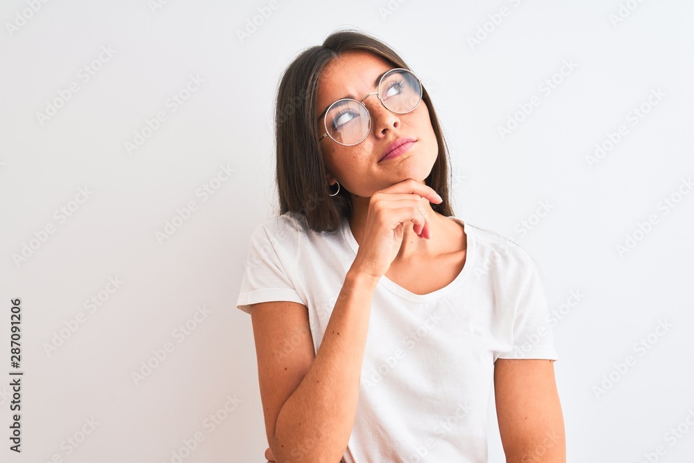 Young beautiful woman wearing casual t-shirt and glasses over isolated white background with hand on chin thinking about question, pensive expression. Smiling with thoughtful face. Doubt concept. Young beautiful woman wearing casual t-shirt and glasses over isolated white background with hand on chin thinking about question, pensive expression. Smiling with thoughtful face. Doubt concept.