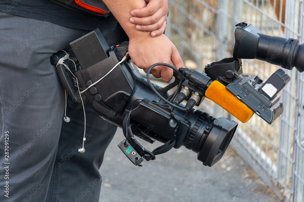Video camera in the hands of a man close-up. The camera operator works with his equipment. Concept: reportage shooting, news, work of journalists.