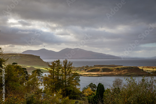Looking out over the harbor of Oban with dark overcast skies and bright sunlight highlighting some land in Oban, Argyll and Bute, Scotland, United Kingdom