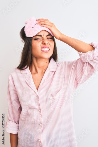 Young beautiful woman wearing sleep mask and pajama over isolated white background stressed with hand on head, shocked with shame and surprise face, angry and frustrated. Fear and upset for mistake.