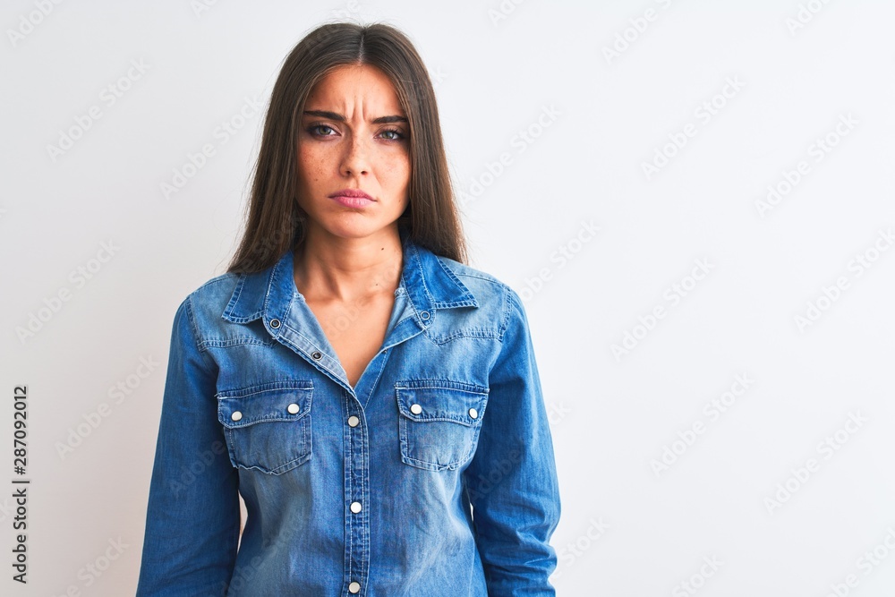 Young beautiful woman wearing casual denim shirt standing over isolated white background skeptic and nervous, frowning upset because of problem. Negative person. Young beautiful woman wearing casual denim shirt standing over isolated white background skeptic and nervous, frowning upset because of problem. Negative person.