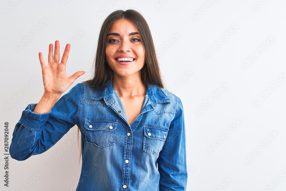 Young beautiful woman wearing casual denim shirt standing over isolated white background showing and pointing up with fingers number five while smiling confident and happy. Young beautiful woman wearing casual denim shirt standing over isolated white background showing and pointing up with fingers number five while smiling confident and happy.