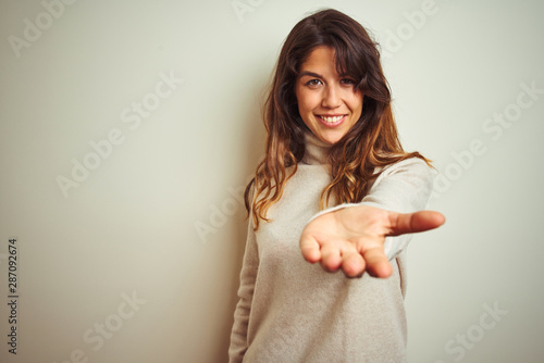 Принти на полотні Young beautiful woman wearing winter sweater standing over white isolated background smiling cheerful offering palm hand giving assistance and acceptance