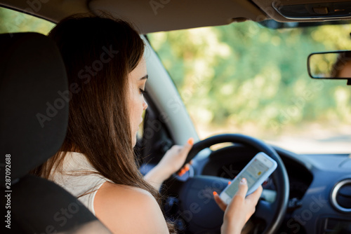 Young female student texting writing messages while driwing a car and doesn`t control the situation. Dangerous driving, addiction to socil medias