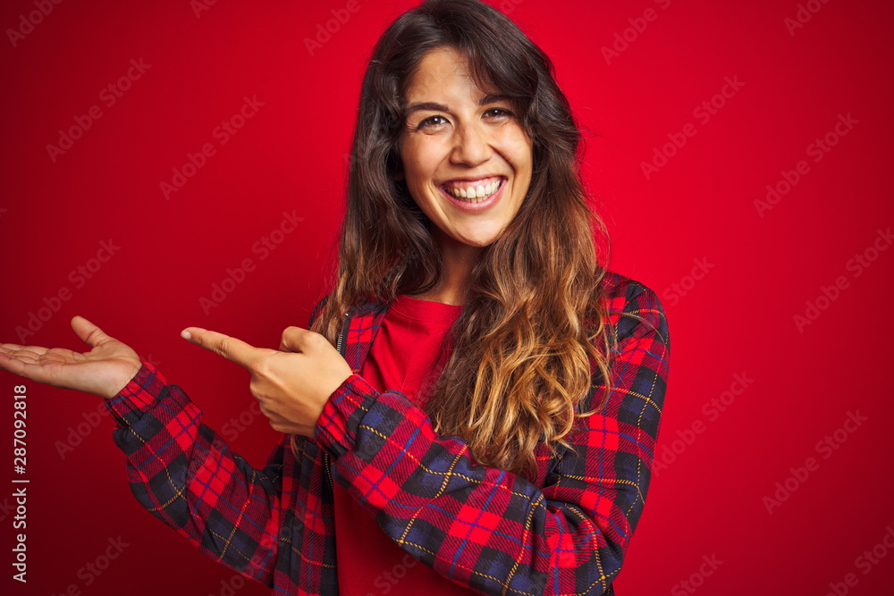 Young beautiful woman wearing casual jacket standing over red isolated background Inviting to enter smiling natural with open hand Young beautiful woman wearing casual jacket standing over red isolated background Inviting to enter smiling natural with open hand