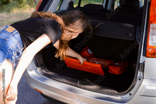 Young beautiful girl puts some things to the car trunk of a modern silver car