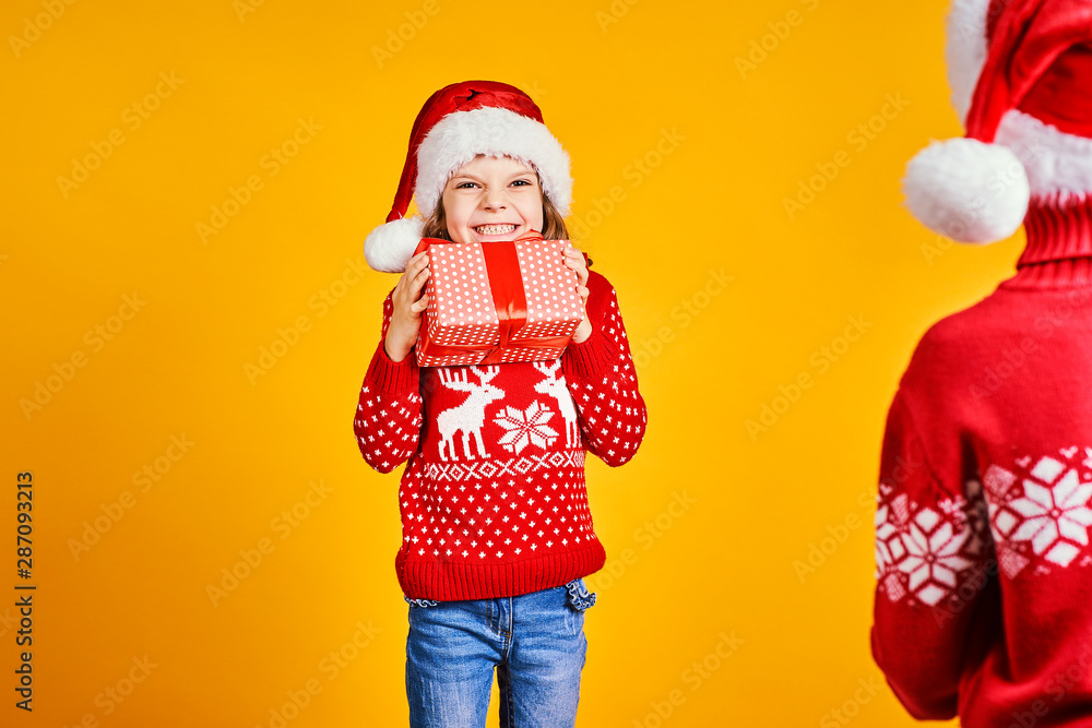 Cheerful kids in Santa hats and red sweaters standing with presents in gift boxes on yellow background Cheerful kids in Santa hats and red sweaters standing with presents in gift boxes on yellow background