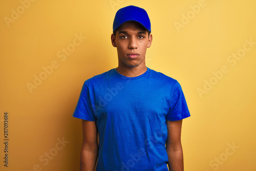 Young handsome arab delivery man standing over isolated yellow background Relaxed with serious expression on face. Simple and natural looking at the camera.