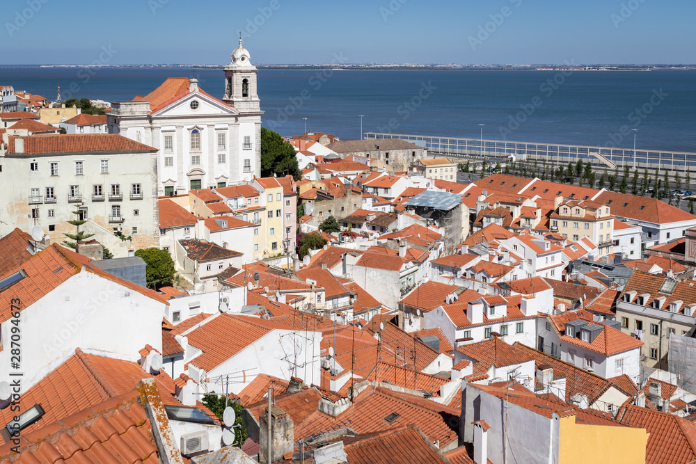 Fototapeta premium View of historic Alfama district in Lisbon, capital of Portugal on a sunny day. Church of Santo Estevao and Tagus river in background