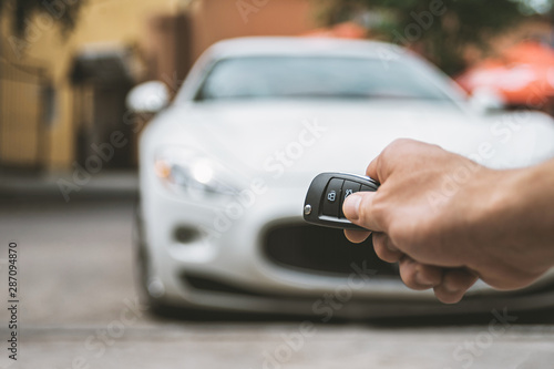 The man opens the car with a keychain, in the background is a white car.
