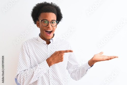 Young african american man wearing elegant shirt and glasses over isolated white background amazed and smiling to the camera while presenting with hand and pointing with finger.