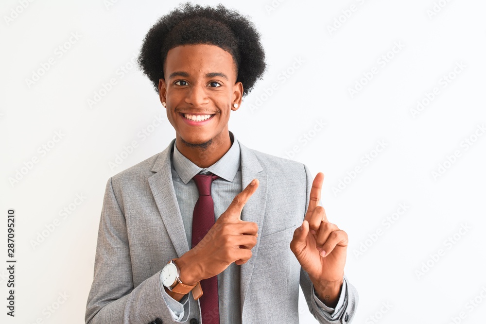 Young african american businessman wearing suit standing over isolated white background smiling and looking at the camera pointing with two hands and fingers to the side. Young african american businessman wearing suit standing over isolated white background smiling and looking at the camera pointing with two hands and fingers to the side.
