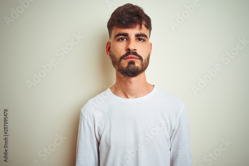 Young man with tattoo wearing t-shirt standing over isolated white background Relaxed with serious expression on face. Simple and natural looking at the camera.
