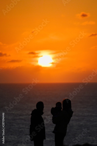 The silhouette of a family  mother  father and son   watching the sunset  intentionally unfocused   at a cliff by the ocean