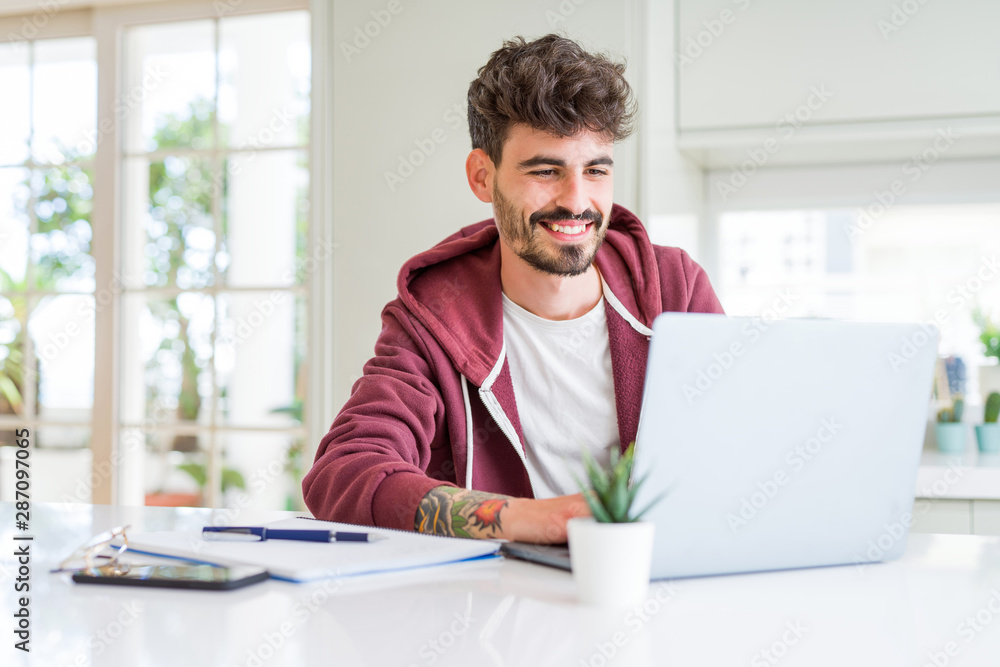 Young student man using computer laptop and notebook with a happy face standing and smiling with a confident smile showing teeth Young student man using computer laptop and notebook with a happy face standing and smiling with a confident smile showing teeth