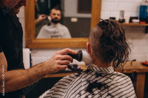 Making perfect haircut look. Young bearded man getting haircut by hairdresser while sitting in chair at barbershop