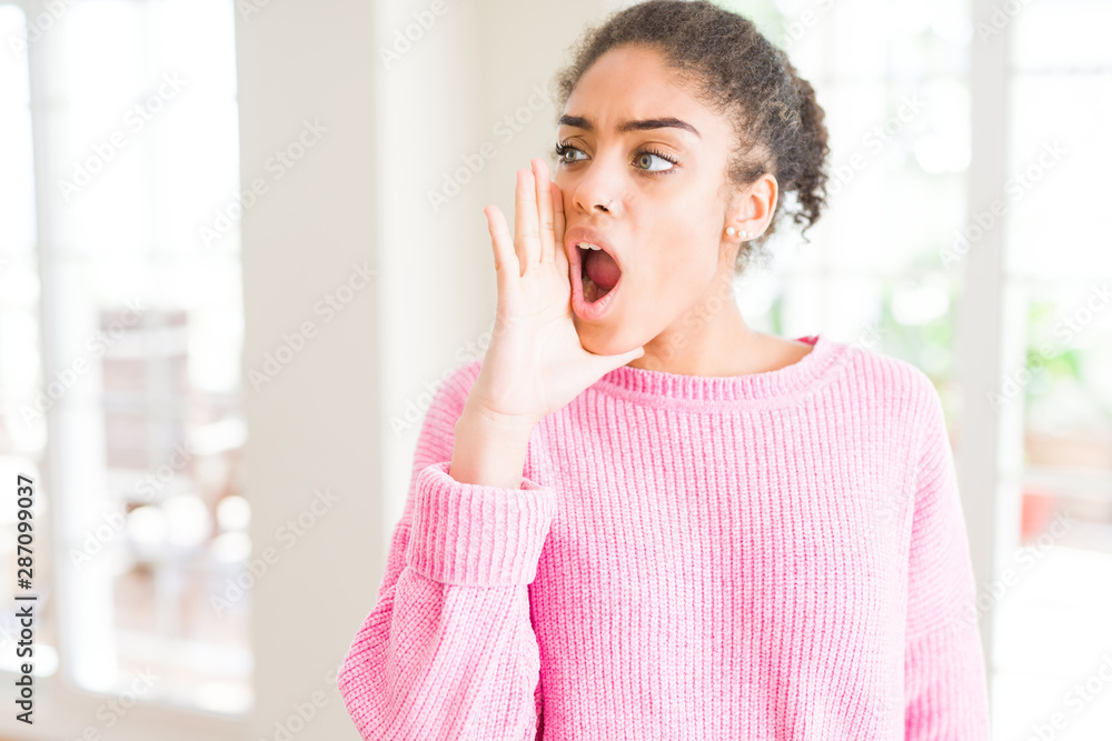 Beautiful young african american woman with afro hair shouting and screaming loud to side with hand on mouth. Communication concept. Beautiful young african american woman with afro hair shouting and screaming loud to side with hand on mouth. Communication concept.