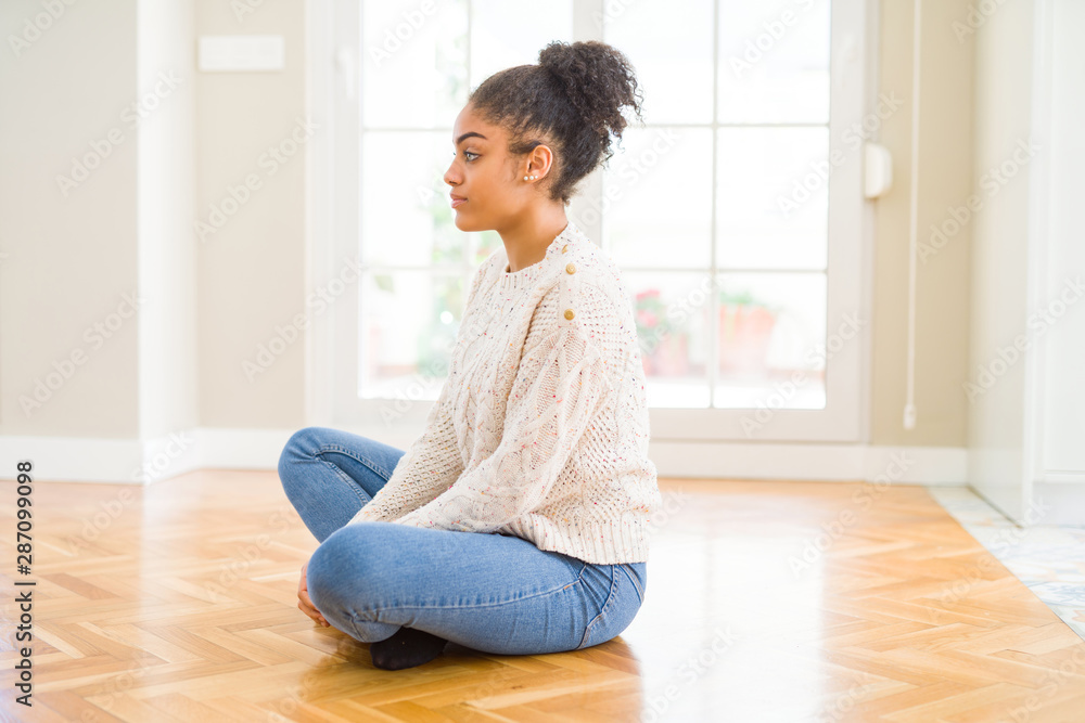 Beautiful young african american woman with afro hair sitting on the floor looking to side, relax profile pose with natural face with confident smile. Beautiful young african american woman with afro hair sitting on the floor looking to side, relax profile pose with natural face with confident smile.