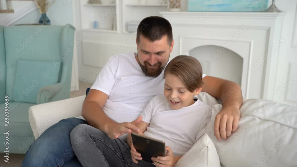 Father and son play together at the tablet and laughing . Family teamwork. Father and son play together at the tablet and laughing . Family teamwork.