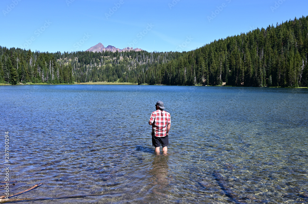 Fototapeta premium Man wading in Todd Lake, Oregon, with Broken Top in background on clear sunny summer afternoon.