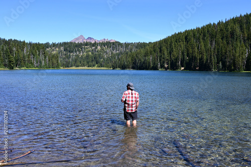 Fotografie Man wading in Todd Lake, Oregon, with Broken Top in background on clear sunny summer afternoon
