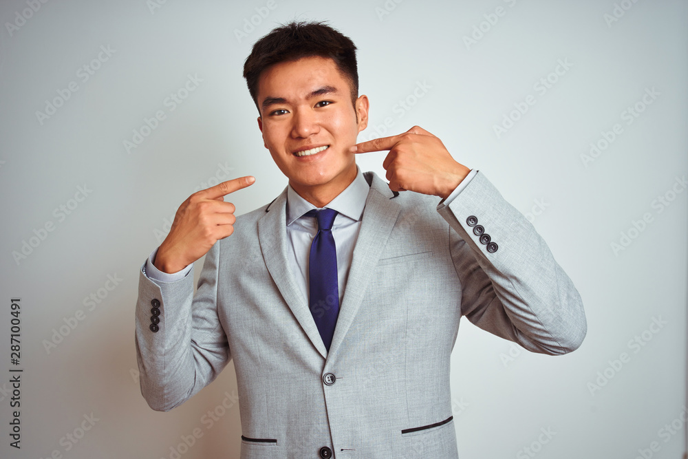 Asian chinese businessman wearing suit and tie standing over isolated yellow background smiling cheerful showing and pointing with fingers teeth and mouth. Dental health concept. Asian chinese businessman wearing suit and tie standing over isolated yellow background smiling cheerful showing and pointing with fingers teeth and mouth. Dental health concept.