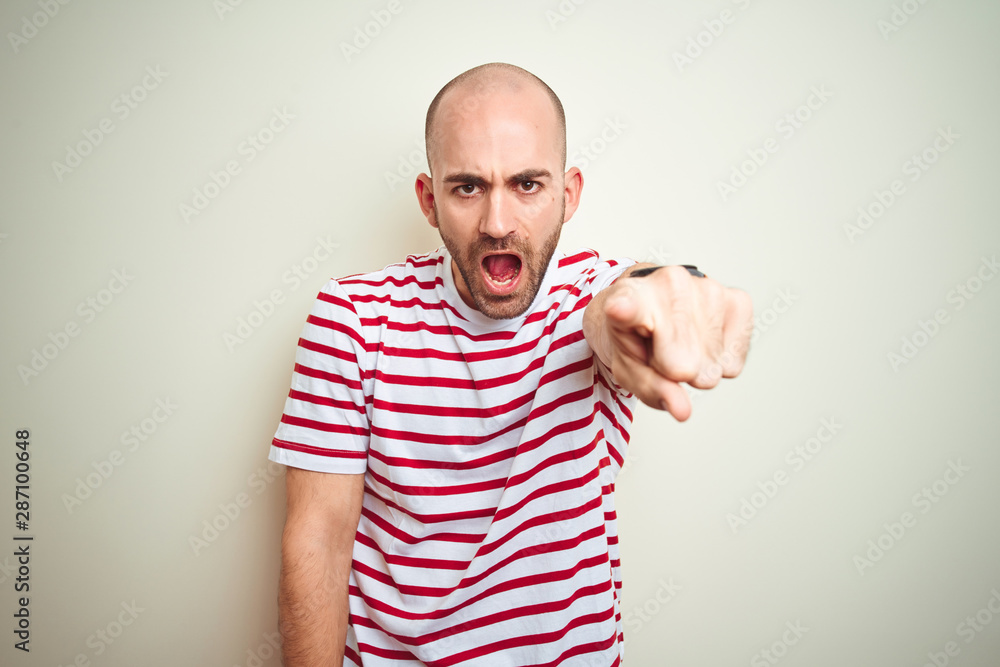 Fototapeta premium Young bald man with beard wearing casual striped red t-shirt over white isolated background pointing displeased and frustrated to the camera, angry and furious with you
