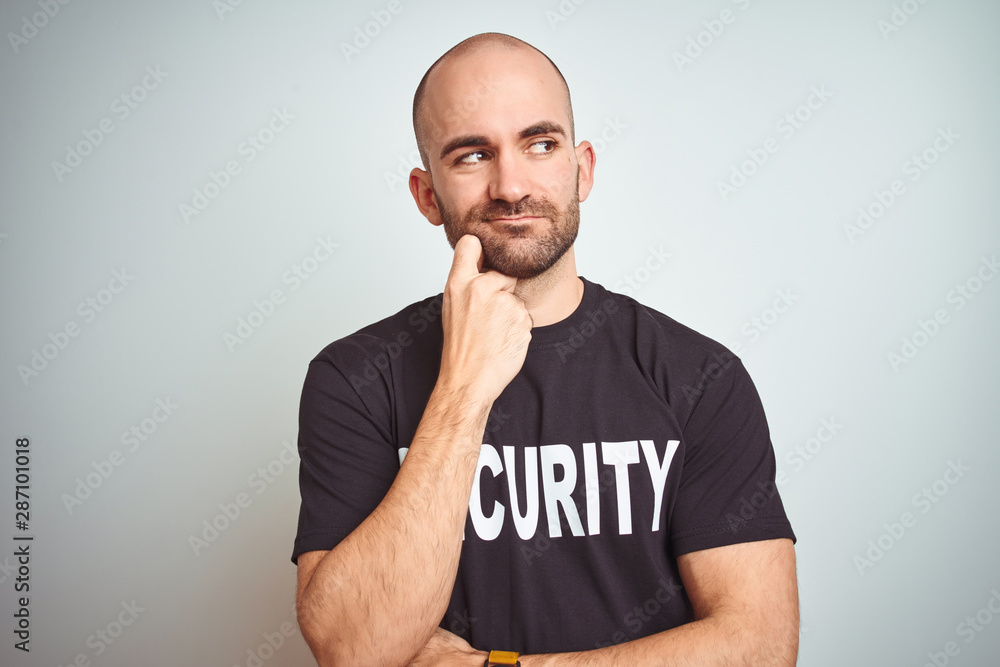Young safeguard man wearing security uniform over isolated background with hand on chin thinking about question, pensive expression. Smiling with thoughtful face. Doubt concept. Young safeguard man wearing security uniform over isolated background with hand on chin thinking about question, pensive expression. Smiling with thoughtful face. Doubt concept.