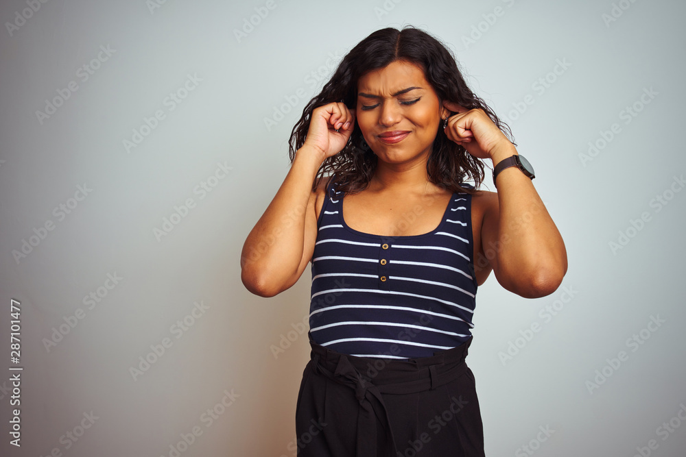 Transsexual transgender woman wearing striped t-shirt over isolated white background covering ears with fingers with annoyed expression for the noise of loud music. Deaf concept. Transsexual transgender woman wearing striped t-shirt over isolated white background covering ears with fingers with annoyed expression for the noise of loud music. Deaf concept.