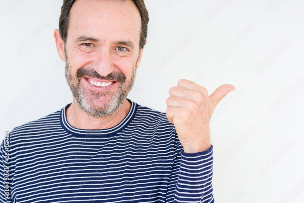 Handsome senior man over isolated background smiling with happy face looking and pointing to the side with thumb up. Handsome senior man over isolated background smiling with happy face looking and pointing to the side with thumb up.