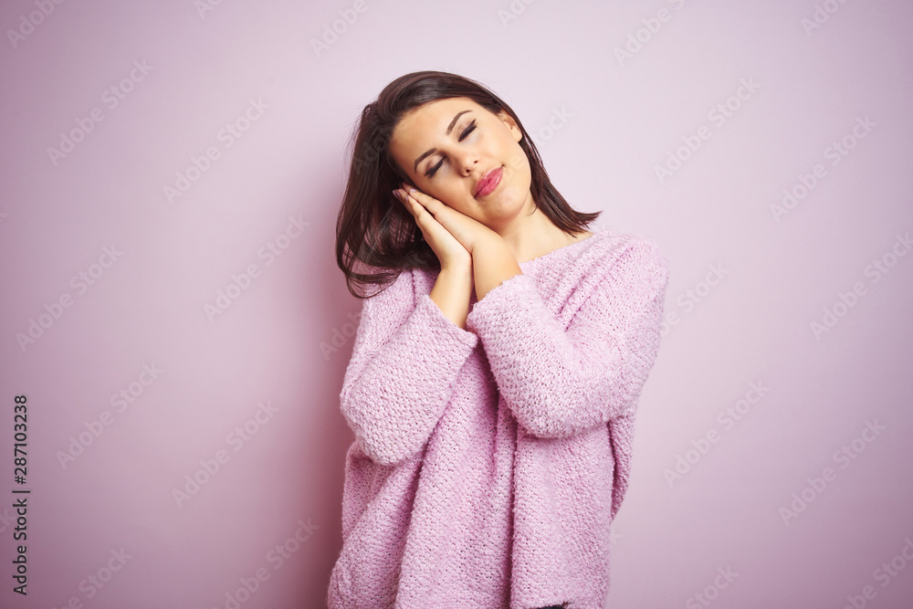 Young beautiful brunette woman wearing a sweater over pink isolated background sleeping tired dreaming and posing with hands together while smiling with closed eyes. Young beautiful brunette woman wearing a sweater over pink isolated background sleeping tired dreaming and posing with hands together while smiling with closed eyes.