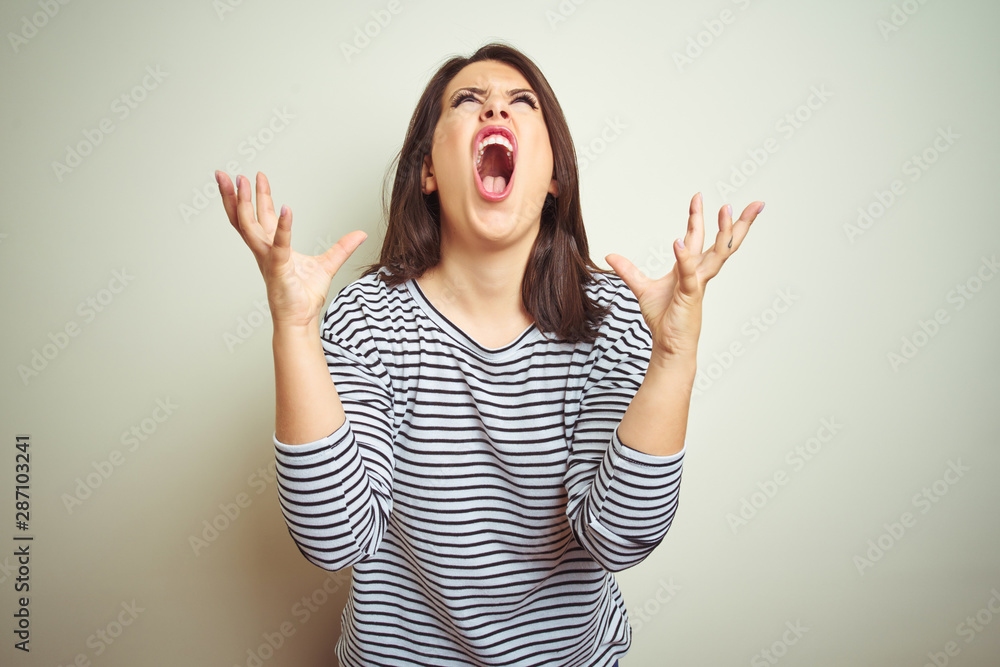 Young beautiful brunette woman wearing striped sweater over white isolated background crazy and mad shouting and yelling with aggressive expression and arms raised. Frustration concept. Young beautiful brunette woman wearing striped sweater over white isolated background crazy and mad shouting and yelling with aggressive expression and arms raised. Frustration concept.