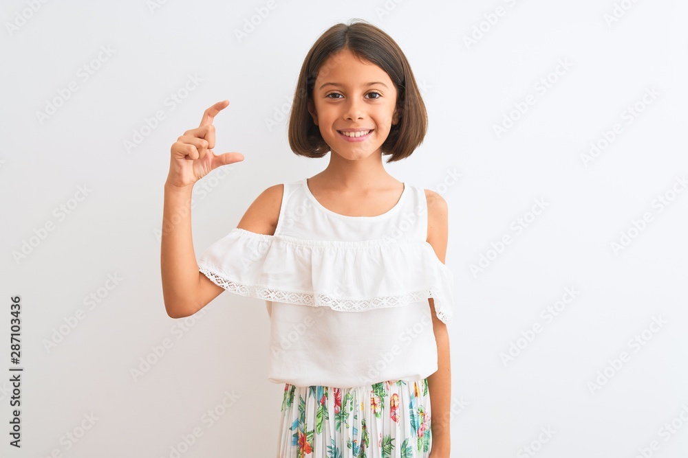 Young beautiful child girl wearing casual dress standing over isolated white background smiling and confident gesturing with hand doing small size sign with fingers looking and the camera Young beautiful child girl wearing casual dress standing over isolated white background smiling and confident gesturing with hand doing small size sign with fingers looking and the camera