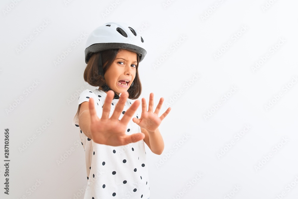 Beautiful child girl wearing security bike helmet standing over isolated white background afraid and terrified with fear expression stop gesture with hands, shouting in shock. Panic concept. Beautiful child girl wearing security bike helmet standing over isolated white background afraid and terrified with fear expression stop gesture with hands, shouting in shock. Panic concept.