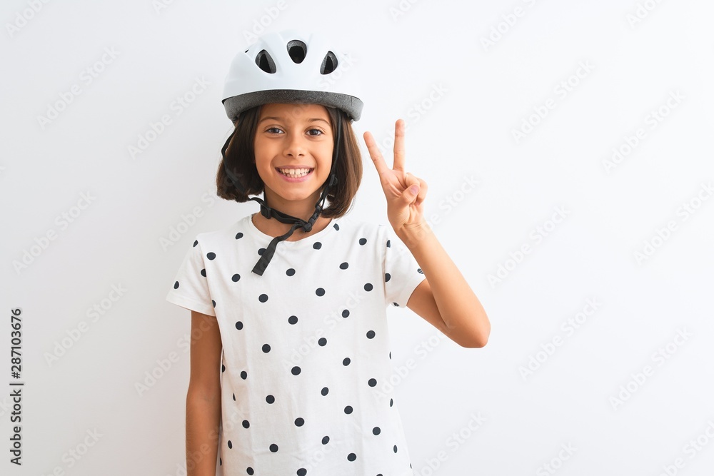 Beautiful child girl wearing security bike helmet standing over isolated white background showing and pointing up with fingers number two while smiling confident and happy. Beautiful child girl wearing security bike helmet standing over isolated white background showing and pointing up with fingers number two while smiling confident and happy.