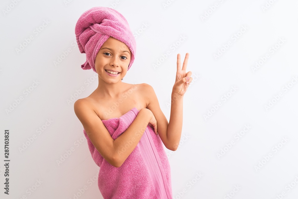 Beautiful child girl wearing shower towel after bath standing over isolated white background smiling with happy face winking at the camera doing victory sign. Number two. Beautiful child girl wearing shower towel after bath standing over isolated white background smiling with happy face winking at the camera doing victory sign. Number two.