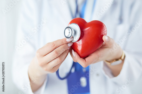 A doctor with stethoscope examining red heart, isolated on white background photo