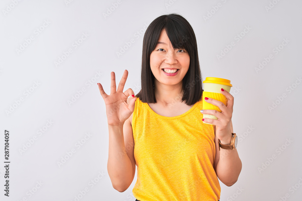 Young beautiful Chinese woman drinking take away coffee over isolated white background doing ok sign with fingers, excellent symbol Young beautiful Chinese woman drinking take away coffee over isolated white background doing ok sign with fingers, excellent symbol