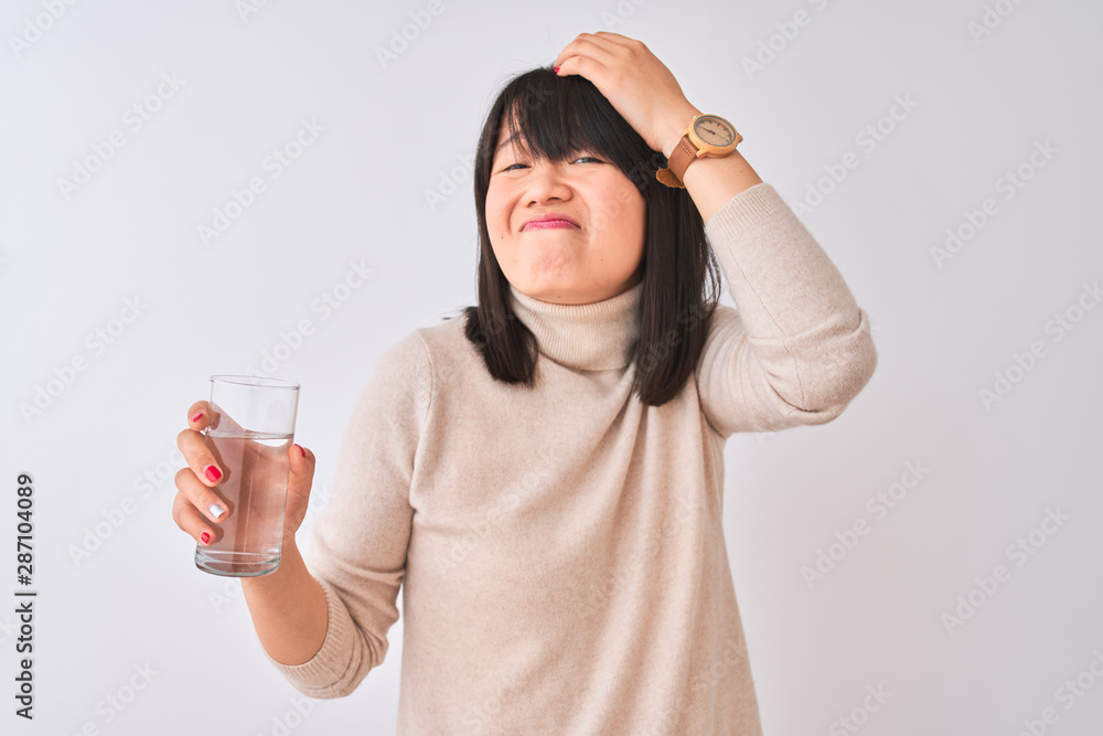 Young beautiful Chinese woman holding glass of water over isolated white background stressed with hand on head, shocked with shame and surprise face, angry and frustrated. Fear and upset for mistake. Young beautiful Chinese woman holding glass of water over isolated white background stressed with hand on head, shocked with shame and surprise face, angry and frustrated. Fear and upset for mistake.
