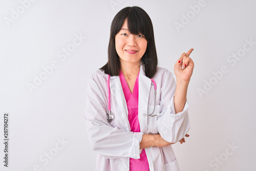 Young beautiful chinese doctor woman wearing stethoscope over isolated white background with a big smile on face  pointing with hand and finger to the side looking at the camera.
