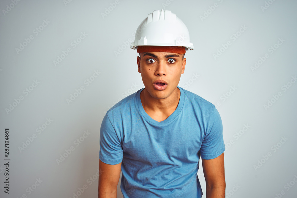 Young brazilian engineer man wearing security helmet standing over isolated white background afraid and shocked with surprise expression, fear and excited face.