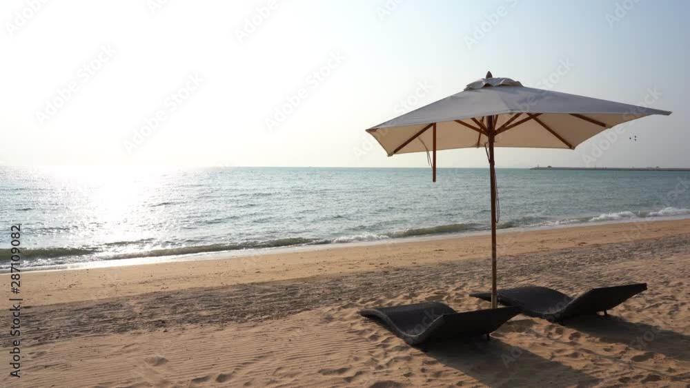 A single shade umbrella stretches out over to sun loungers while waves rolling to the shore. A single shade umbrella stretches out over to sun loungers while waves rolling to the shore.
