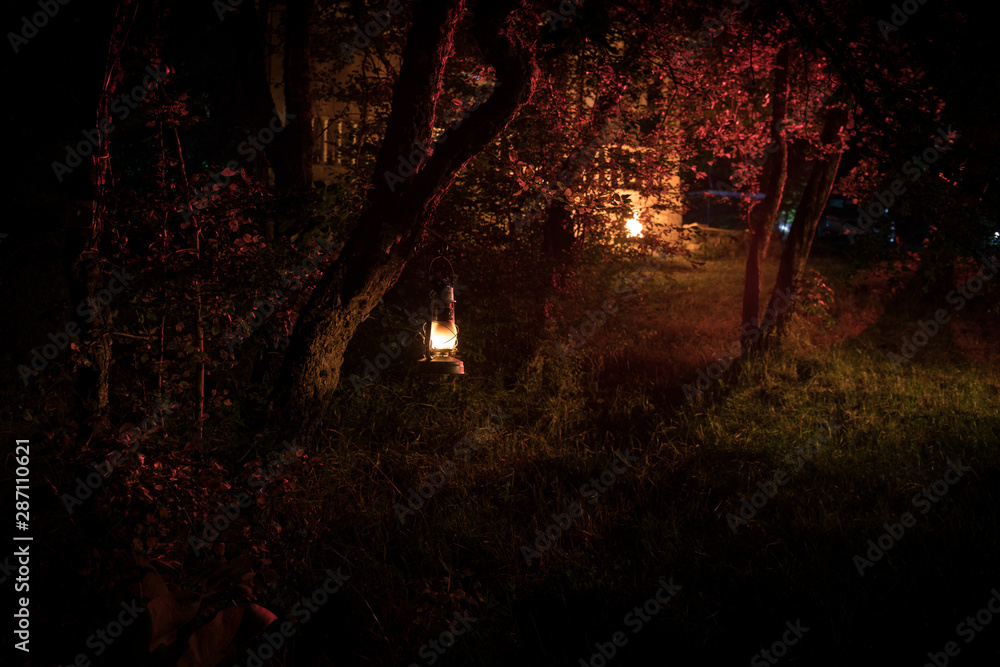 Fototapeta premium Horror Halloween concept. Burning old oil lamp in forest at night. Night scenery of a nightmare scene.