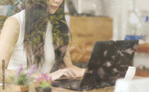 Cropped image through glass window of  beautiful Asian business woman with long black hair working in cafe