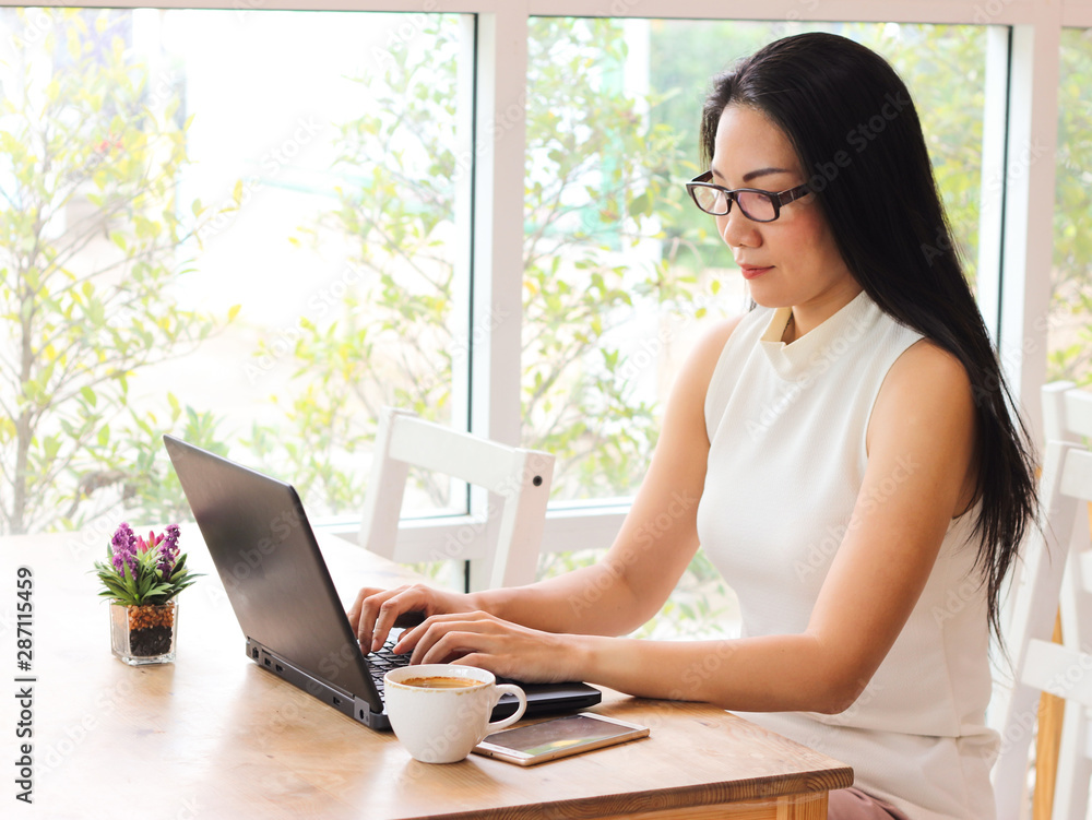 Asian business woman with long black hair wearing eye glasses working in coffee shop , typing on computer Asian business woman with long black hair wearing eye glasses working in coffee shop , typing on computer