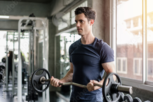 Handsome weightlifter lifting barbells working out with curl bar in the gym