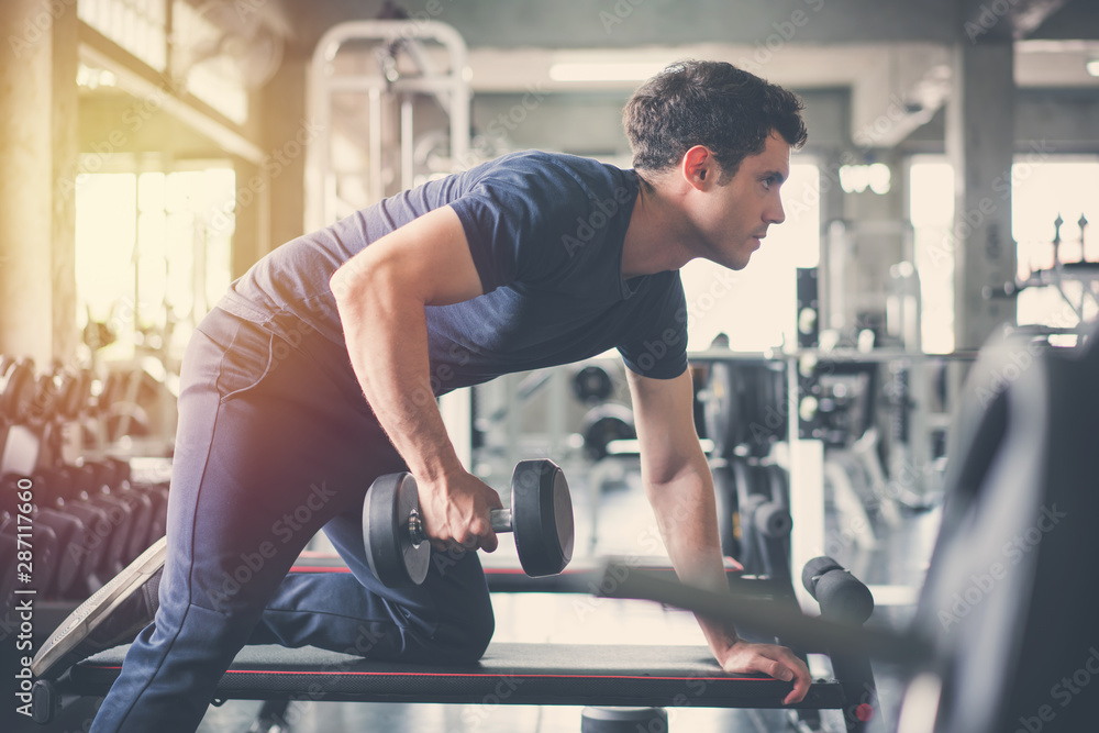 Handsome weightlifter lifting bench press working out with dumbbell in the gym