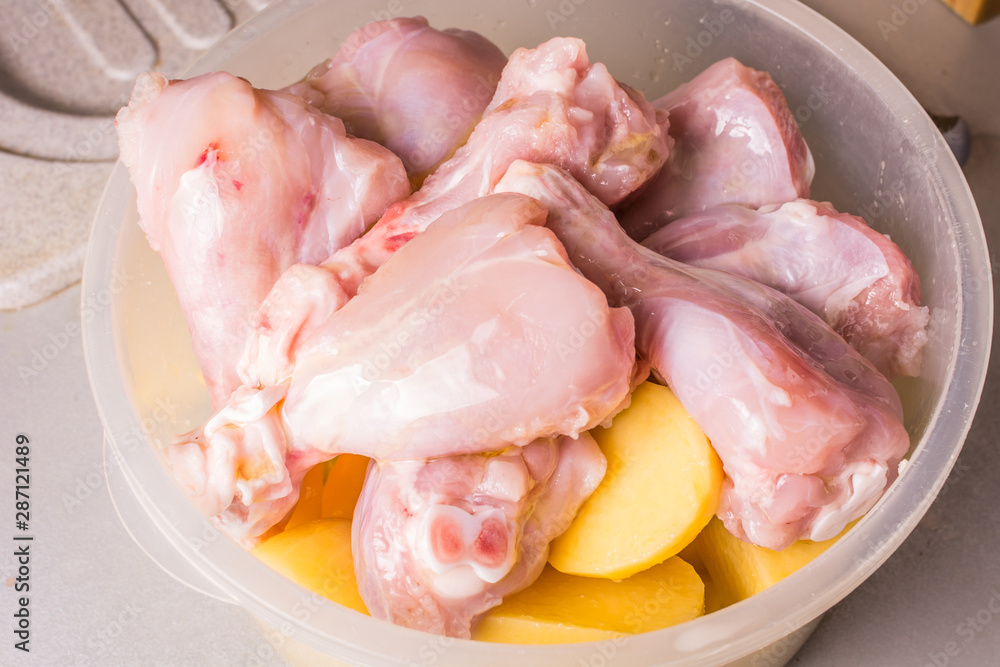Raw chicken legs and sliced potatoes in deep plate cooked for roasting in oven. Raw chicken legs and sliced potatoes in deep plate cooked for roasting in oven.