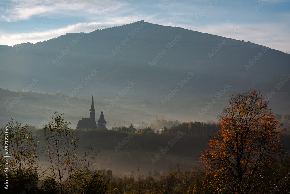 Old wooden church surrounded by fog in the morning in Maramures, Romania