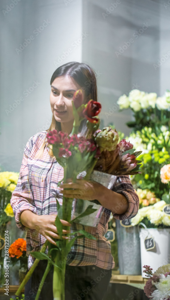 A young girl in a plaid shirt chooses and creates a composition of flowers in a flower shop